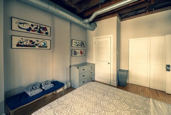 Une chambre à coucher avec un lit, un banc avec des serviettes, une commode et des œuvres d’art accrochées au mur.