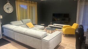 A modern living room with a grey sofa, yellow armchairs, a small coffee table, and a flat-screen TV. - Au délices d'Anne Laure !   (Pleumeur-Gautier)
