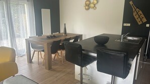 A modern kitchen with a black countertop, a wooden dining table, and black bar stools. - Au délices d'Anne Laure !   (Pleumeur-Gautier)