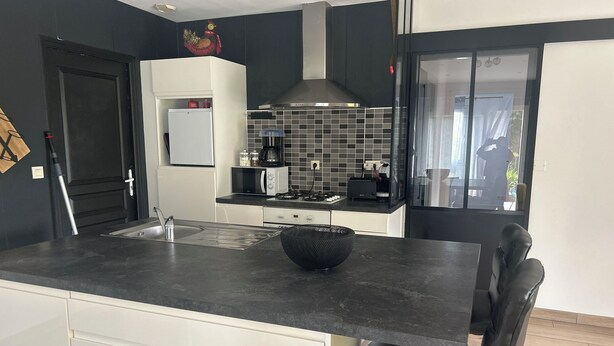 A modern kitchen with a black countertop, white cabinets, a microwave, a coffee maker, and a black chair. - Au délices d'Anne Laure !   (Pleumeur-Gautier)
