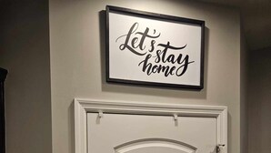 Eine weiße Tür mit einem dekorativen Schild darüber, auf dem steht: 'Lasst uns zu Hause bleiben.'