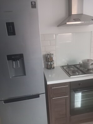 A kitchen with a stainless steel refrigerator, a water dispenser, a gas stove, and a microwave. - Cozy Bromley Hideaway - Perfect for Couples (Bromley)