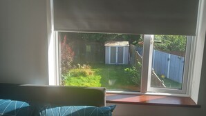 Una camera da letto con un'ampia finestra, un termosifone e un letto con cuscini azzurri.
