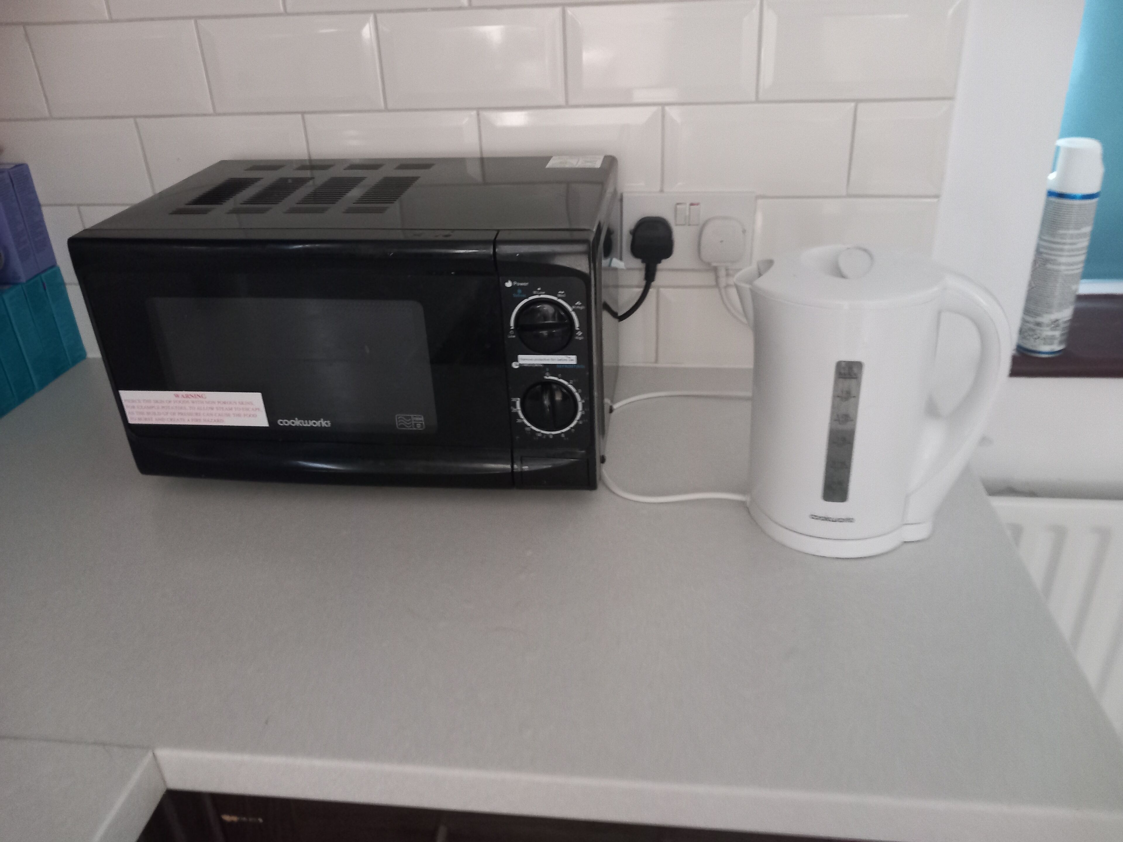 Una cocina con un microondas negro y una tetera eléctrica blanca sobre una encimera.