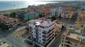 Ett bostadsområde vid kusten med flerfamiljshus, vissa med balkonger, och en strand syns i bakgrunden.