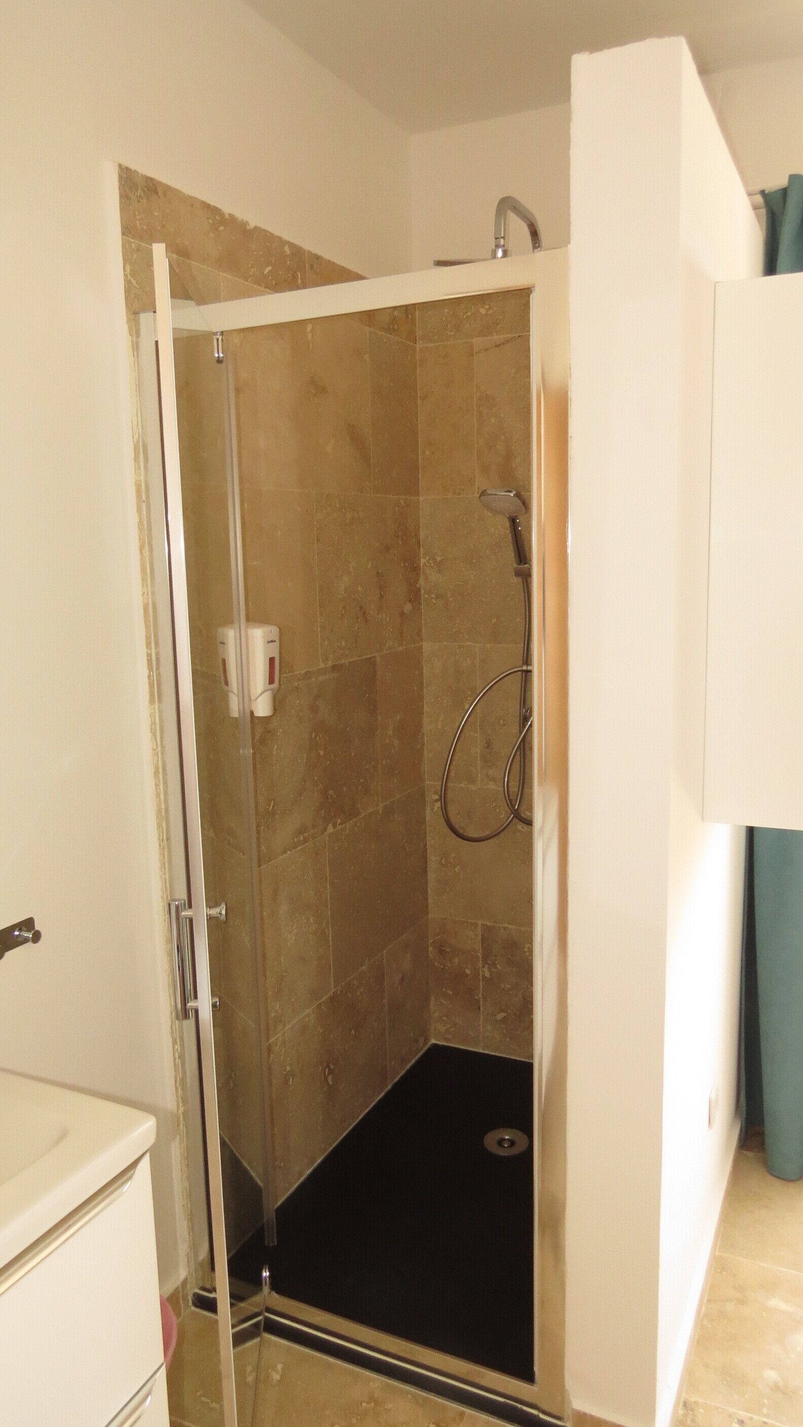 A shower with a glass door, beige tiles, and a black floor.