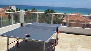 Une table de ping-pong sur un balcon avec vue sur l’océan et les bâtiments.