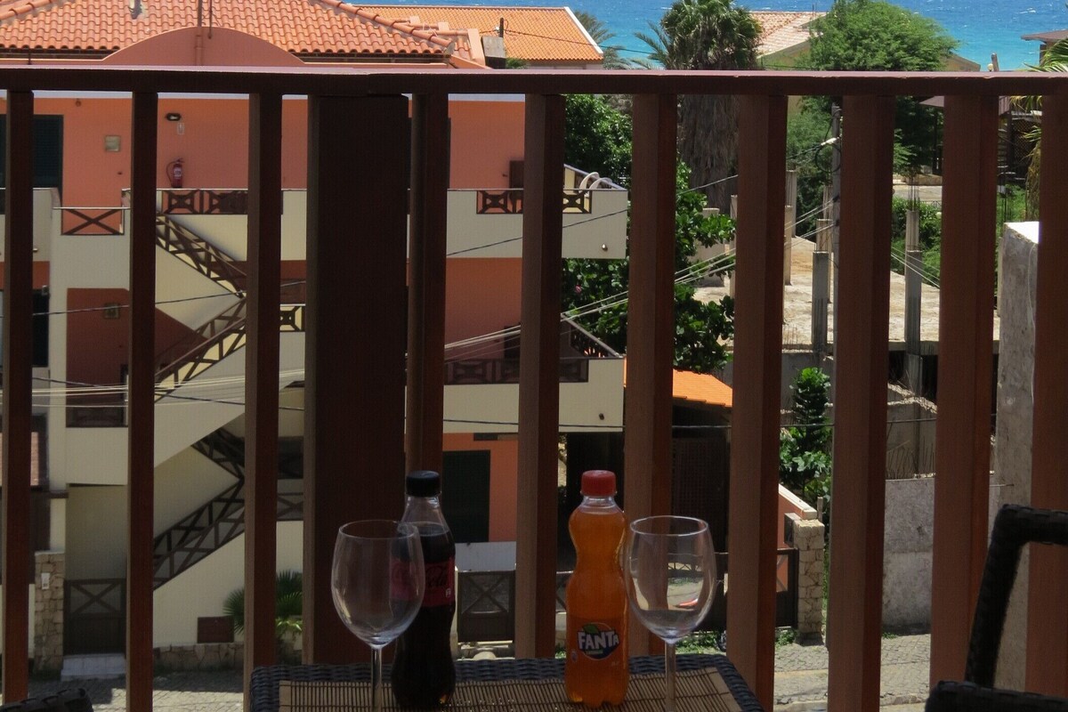 A balcony with a view of the sea, a bottle of Fanta, and two wine glasses.
