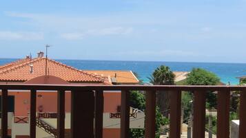 A balcony with a view of the sea, a bottle of Fanta, and two wine glasses.