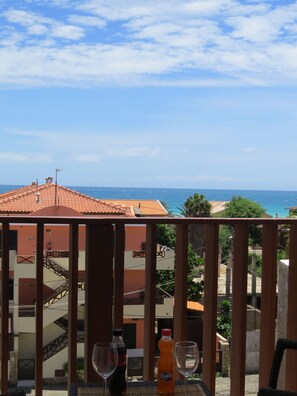 Un balcon avec vue sur la mer, une bouteille de Fanta et deux verres à vin.