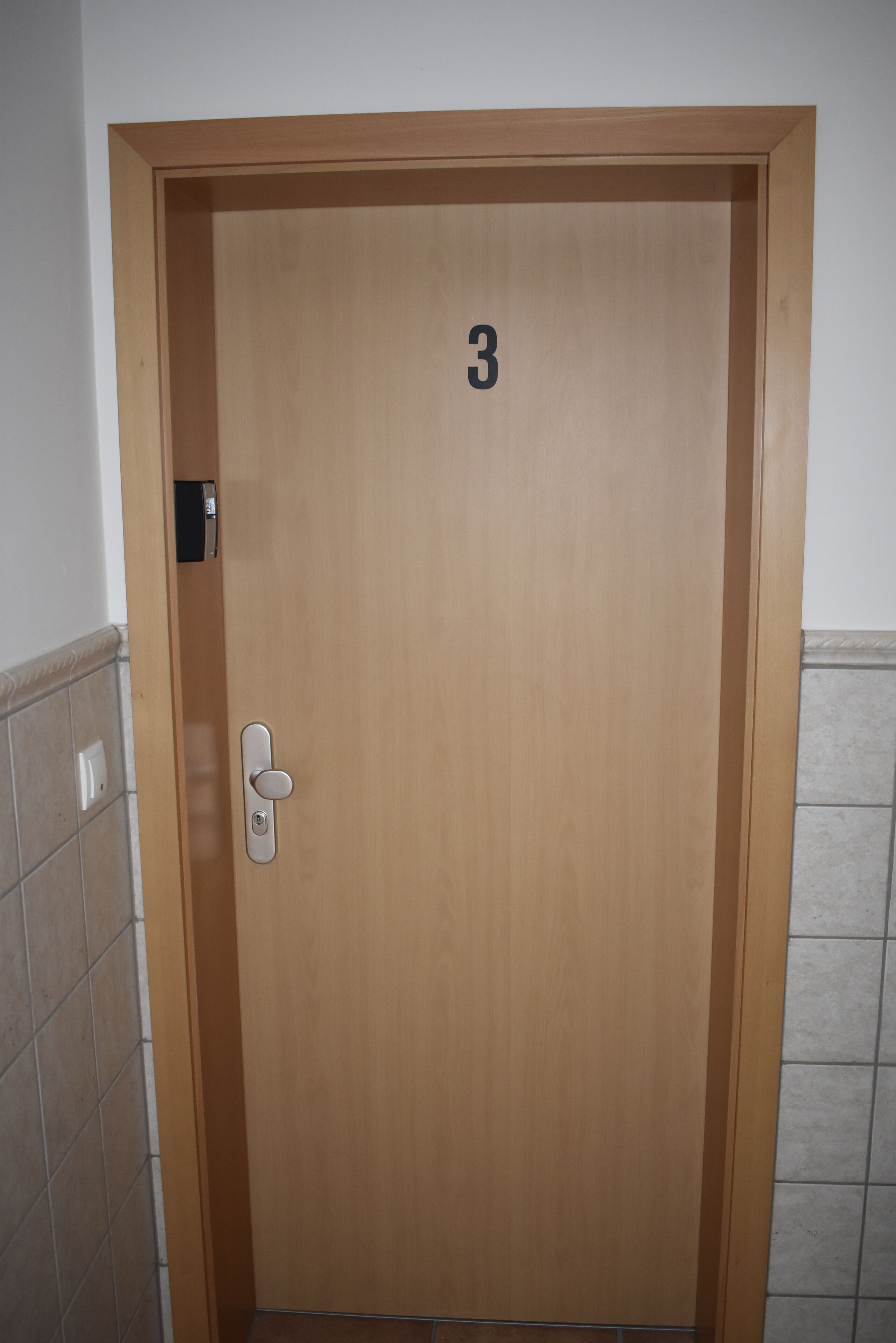 A wooden door with a number "3" on it, a door handle, and a small electronic device mounted on the door.