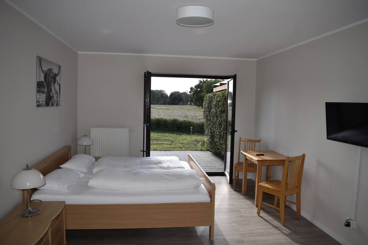 A bedroom with a wooden bed, a bedside table with a lamp, a chair, and a TV mounted on the wall.