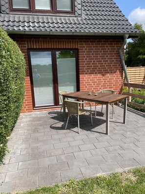 A patio with a table and chairs, a brick wall, and a tiled roof. - Pension zur Schleuse (Witzeeze)