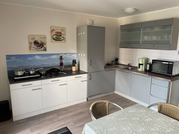 A modern kitchen with a dining area, featuring a stove, sink, and microwave. - Pension zur Schleuse (Witzeeze)