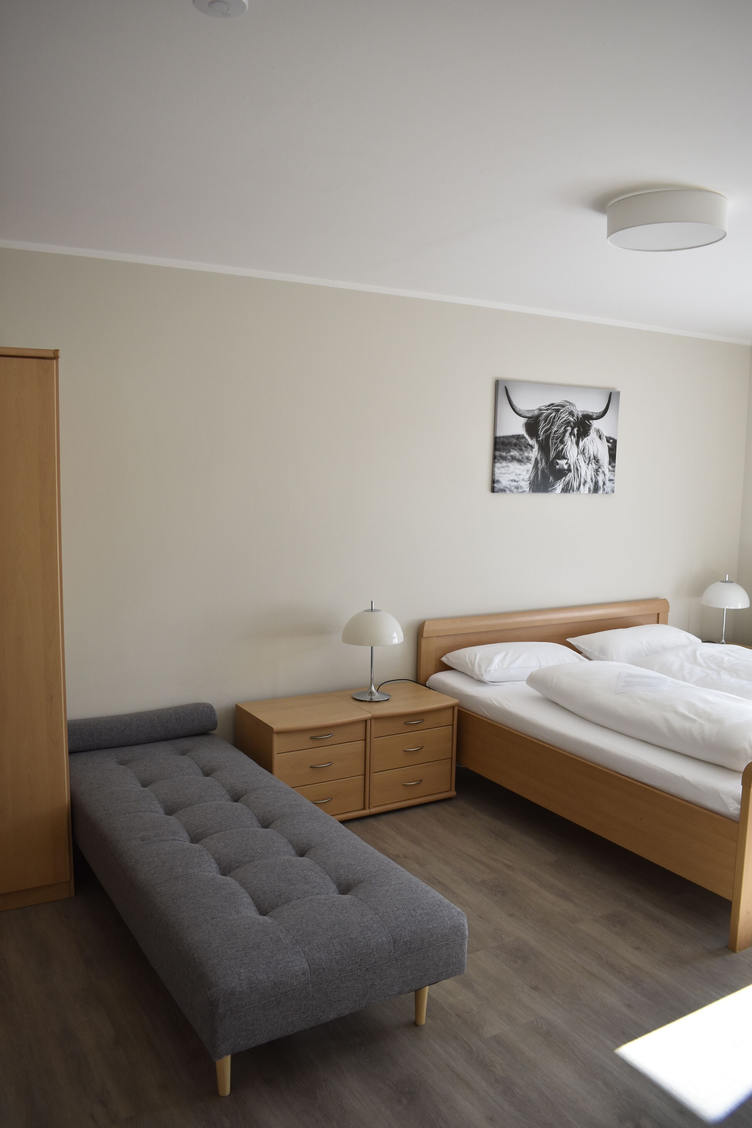 A bedroom with a bed, bedside tables, a bench, and a wall-mounted picture.