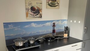 A modern kitchen with a black countertop, white cabinets, and a backsplash depicting a lighthouse and sea view. - Pension zur Schleuse (Witzeeze)