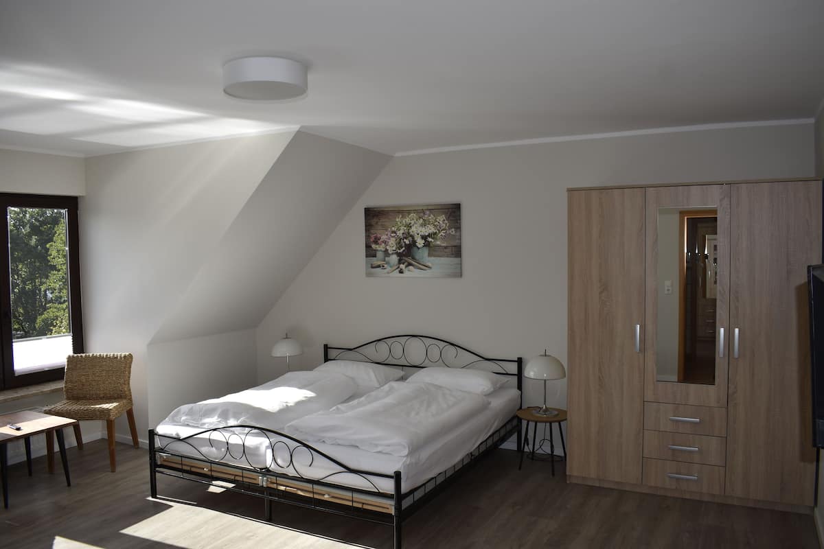 A bedroom with a bed, a chair, a bedside table, a lamp, a wardrobe, and a painting on the wall.