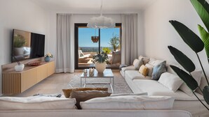 Una sala de estar moderna con sofá, mesa de centro y televisor. Tiene un balcón con vistas.