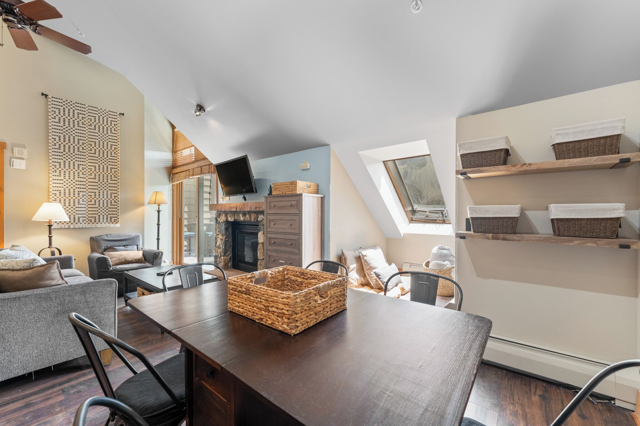A cozy living room with a fireplace, a dining area, and a loft bedroom with a skylight.