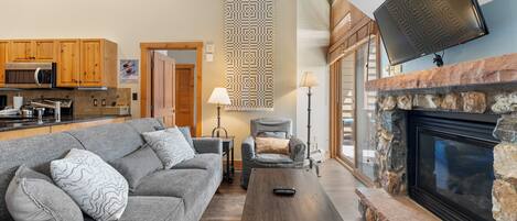 A living room with a gray sofa, a wooden coffee table, a stone fireplace, and a mounted TV.