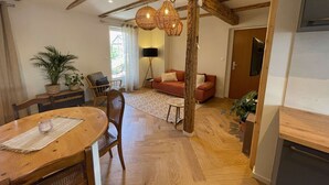 Een gezellige woonkamer met een houten vloer, een bank, een eettafel met stoelen en een hanglamp.