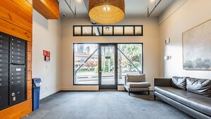 Un espace d’accueil avec un mur en bois, une poubelle bleue, un canapé et une grande fenêtre donnant sur la rue.