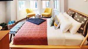 A bedroom with a bed, two yellow chairs, a small table, and a TV mounted on the wall. - 2227 Locust (Philadelphia)