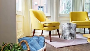 A room with two yellow armchairs, a wicker basket with denim, and a patterned ottoman. - 2227 Locust (Philadelphia)