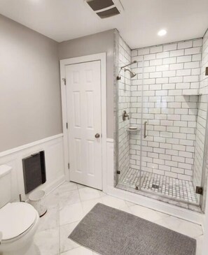Un baño con puerta blanca, cabina de ducha de vidrio y inodoro blanco.