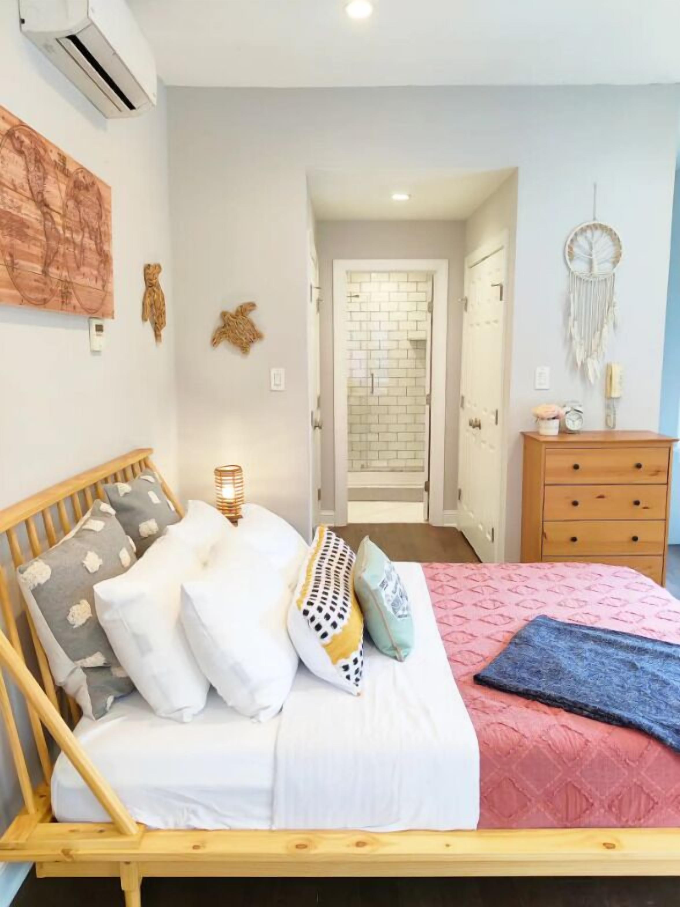 A bedroom with a wooden bed, white bedding, a red quilt, and a wooden dresser.