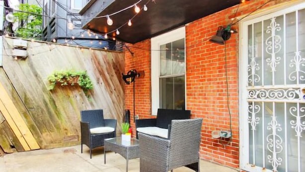 A patio with wicker furniture and string lights, a brick wall, and a decorative metal gate. - 2227 Locust (Philadelphia)