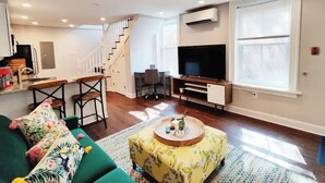 A modern living room with a green sofa, a wooden coffee table, a TV, and a staircase leading to another level. - 2227 Locust (Philadelphia)