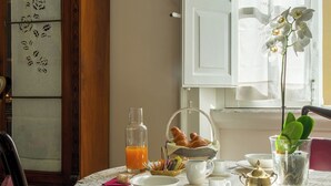 Une table à manger recouverte d’une nappe blanche, un verre de jus d’orange, une théière et une petite plante orchidée.