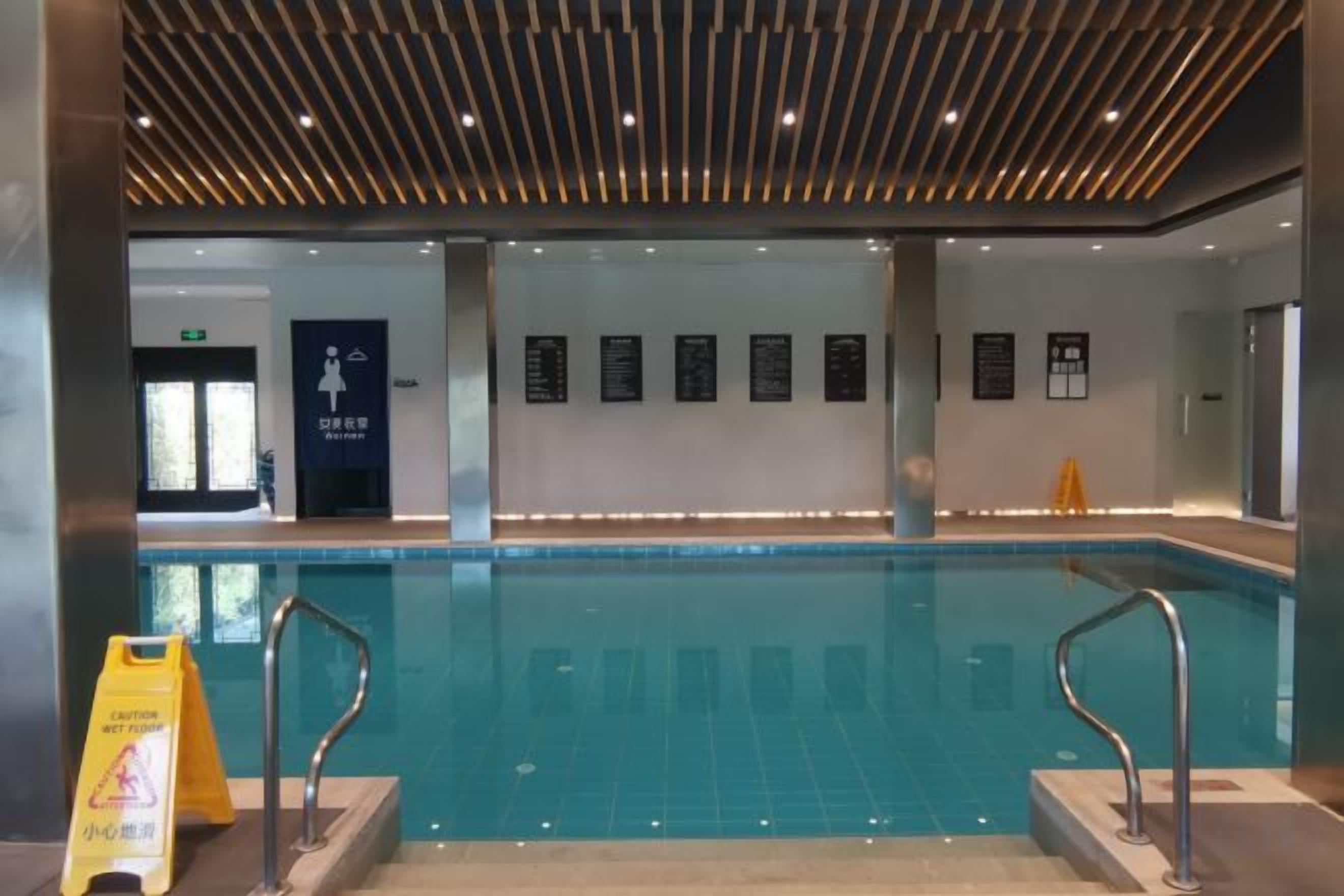 A swimming pool with a tiled floor, metal handrails, and a wooden ceiling.