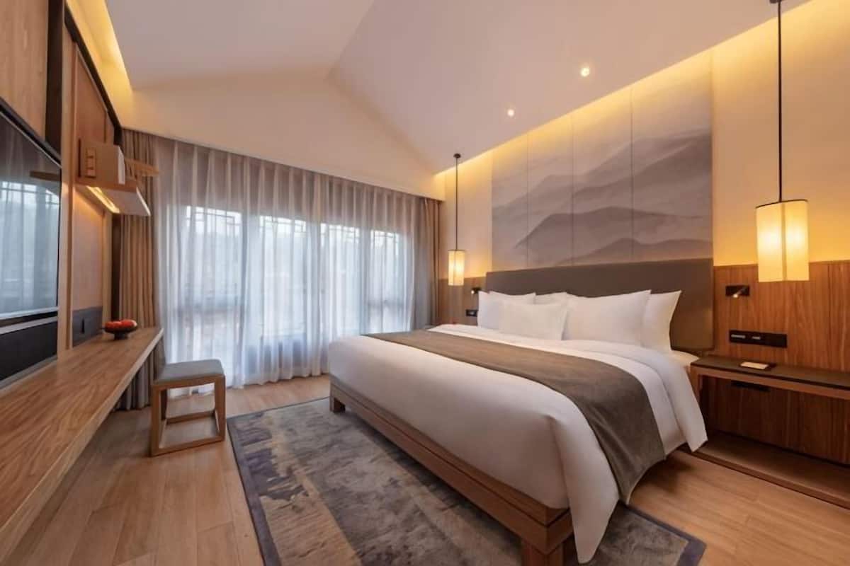 A modern hotel room with a large bed, a desk, and a TV.