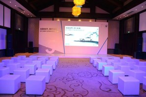 A conference room with a presentation screen, white cube seating, and patterned carpet. - GRAND HOUSE NINGBO (Ningbo)