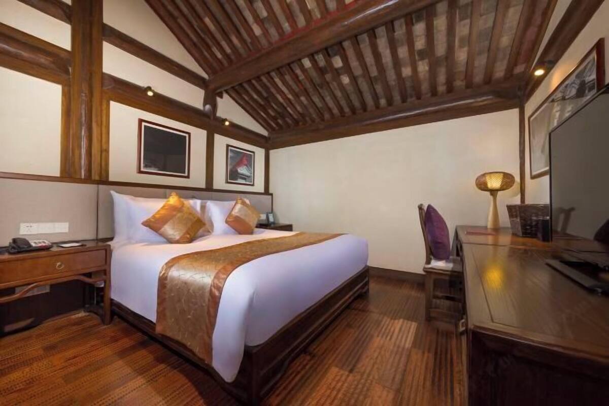 A hotel room with a large bed, wooden ceiling beams, a desk, and a chair.