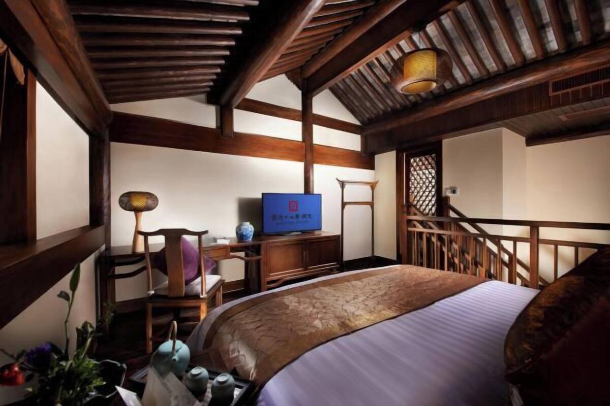A traditional room with a bed, wooden furniture, a television, and a staircase.