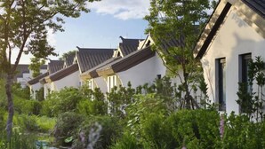 A row of traditional-style buildings with sloped roofs, surrounded by lush greenery and a small water feature. - GRAND HOUSE NINGBO (Ningbo)
