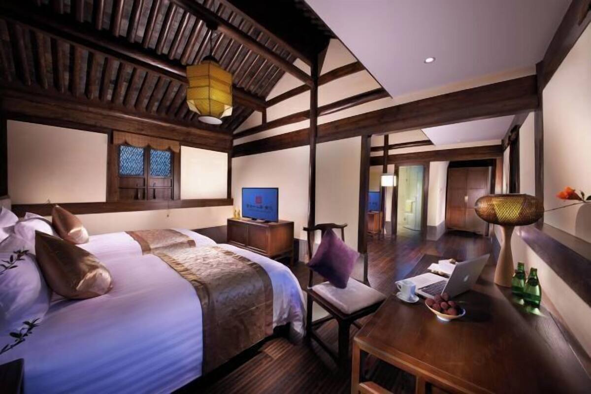 A hotel room with a large bed, a desk with a laptop, a chair, and a small table with bottles.