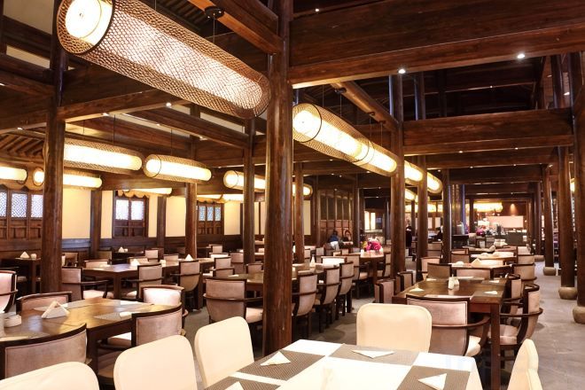 A spacious restaurant with high ceilings and wooden beams, featuring multiple dining tables and chairs.