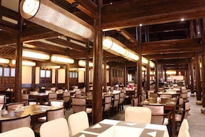 Un restaurant spacieux avec de hauts plafonds et des poutres en bois, comprenant plusieurs tables et chaises.