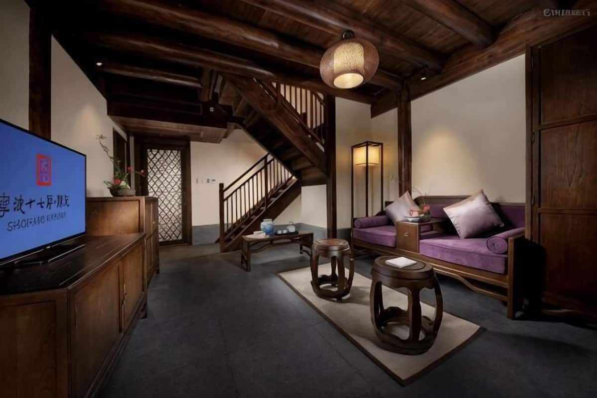 A living room with a TV, wooden furniture, a staircase, and a purple sofa.