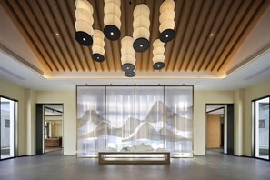 Een ruime lobby met een modern plafondontwerp, een wand met een berglandschap en een bank.