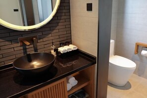 Een moderne badkamer met een zwarte wasbak, een ronde spiegel, een toilet en een handdoekhouder.