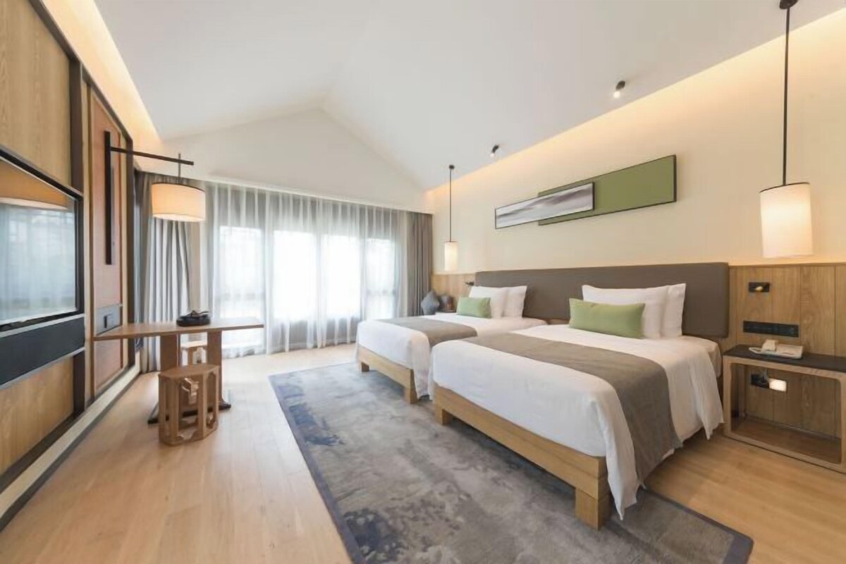 Een moderne hotelkamer met twee bedden, een bureau en een groot raam met gordijnen.