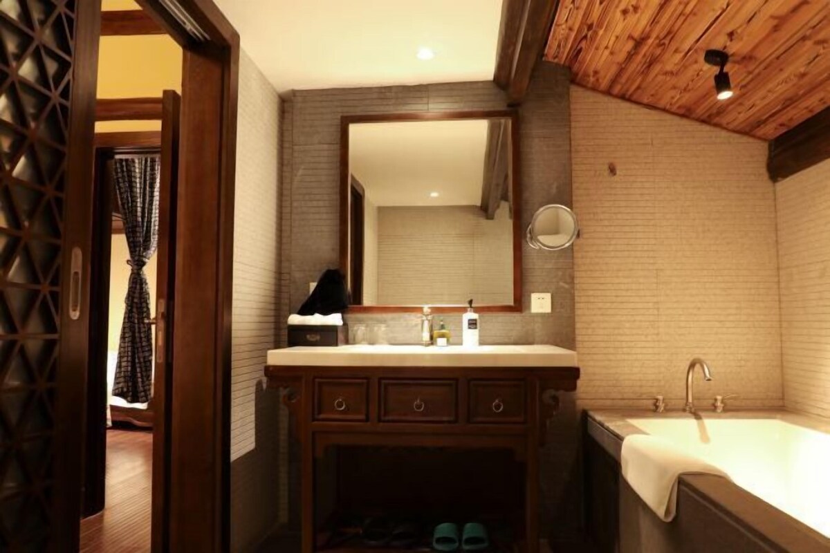 Een badkamer met een houten wastafelmeubel, een grote spiegel, een wastafel en een bad.