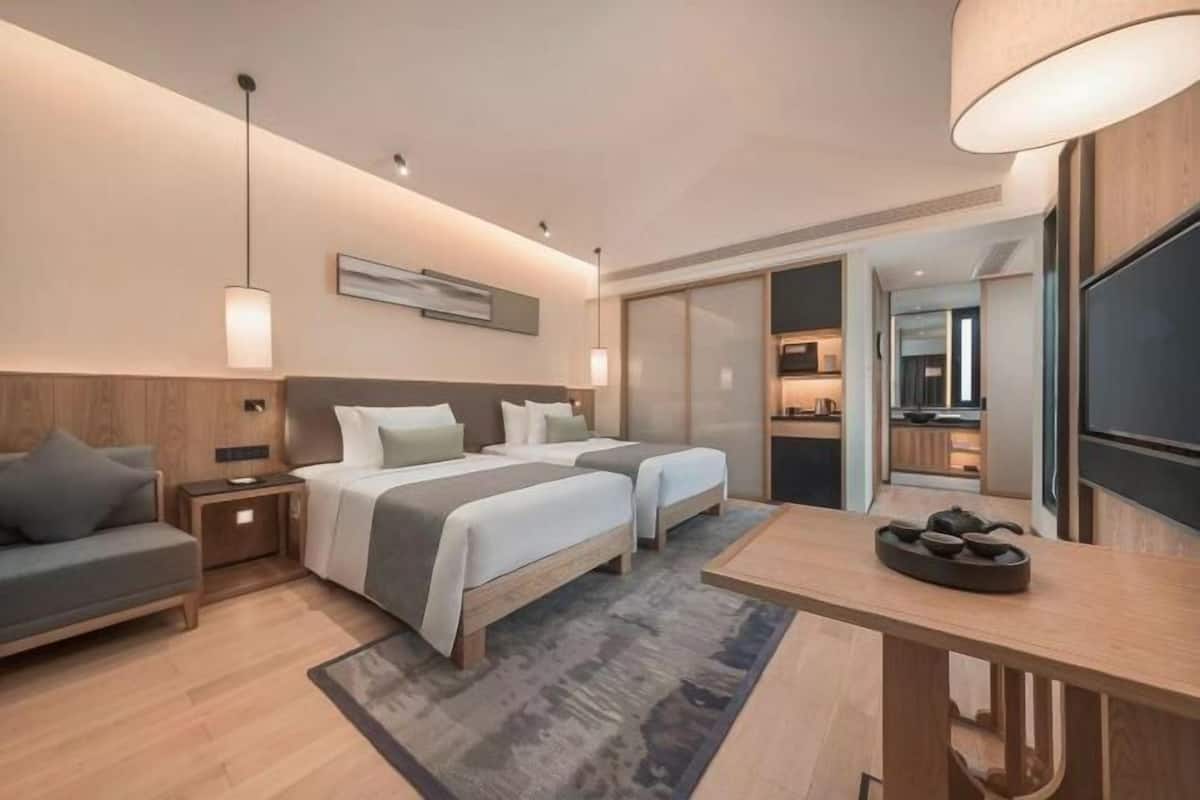 A modern hotel room with two beds, a sofa, a dining table, and a TV.