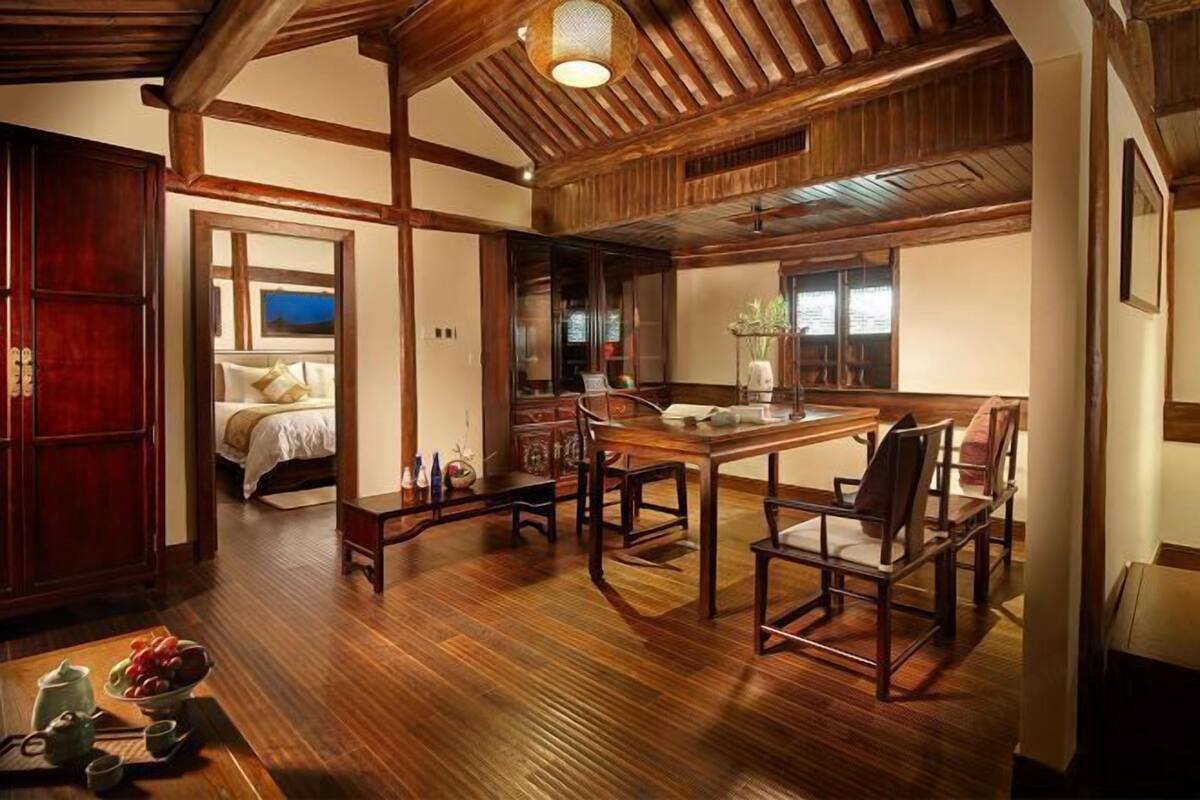 A traditional Japanese-style room with tatami flooring, a low wooden table with chairs, a bed with a view, and a wooden ceiling with exposed beams.