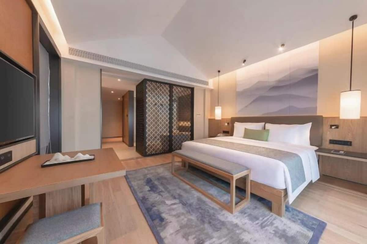 A modern hotel room with a bed, bedside tables, a desk, a bench, a TV, and a decorative wall.